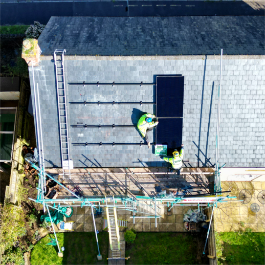 A roof with scaffolding and solar panels is being put on. Two worked in hi-vis jackets with Tincknell solar written on the back, attaching the panels