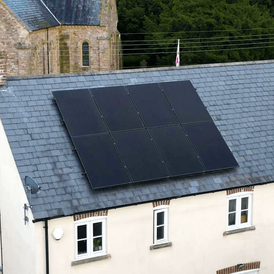 A white-coloured house with grey slate tile roofing, with block solar panels on the top 
